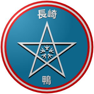 The logo of the Nagasaki Kamo (Ducks): A blue circle, surrounded by red-white-red, on which Nagasaki's emblem of a five-pointed star containing something like stylized snowflake patterns sits between the white characters for "Nagasaki" and for "Kamo."